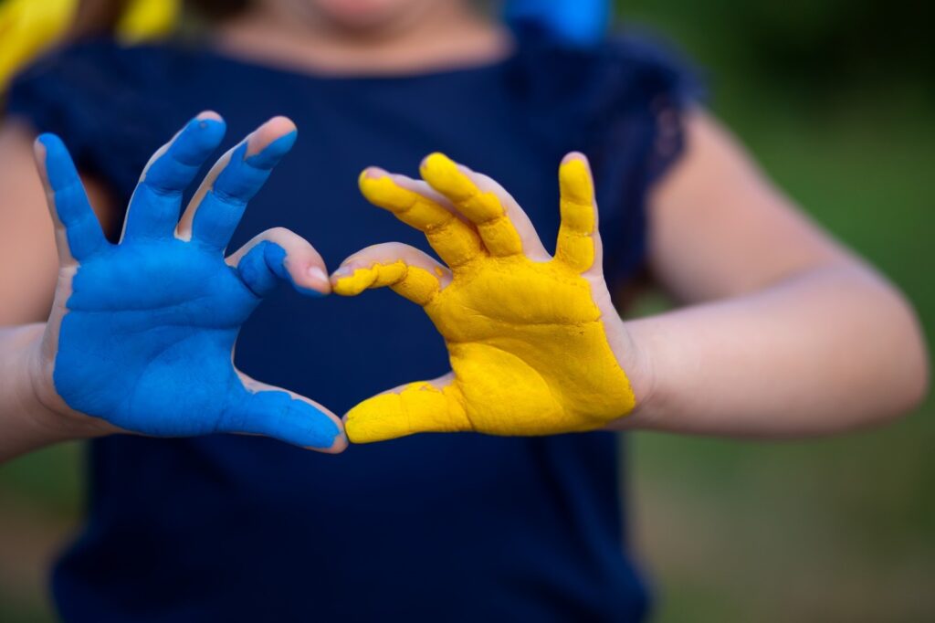 Oekraïne hartje gemaakt met 2 handen. De rechter hand is gekleurd met blauwe verf, de linkerhand is gekleurd met gele verf.